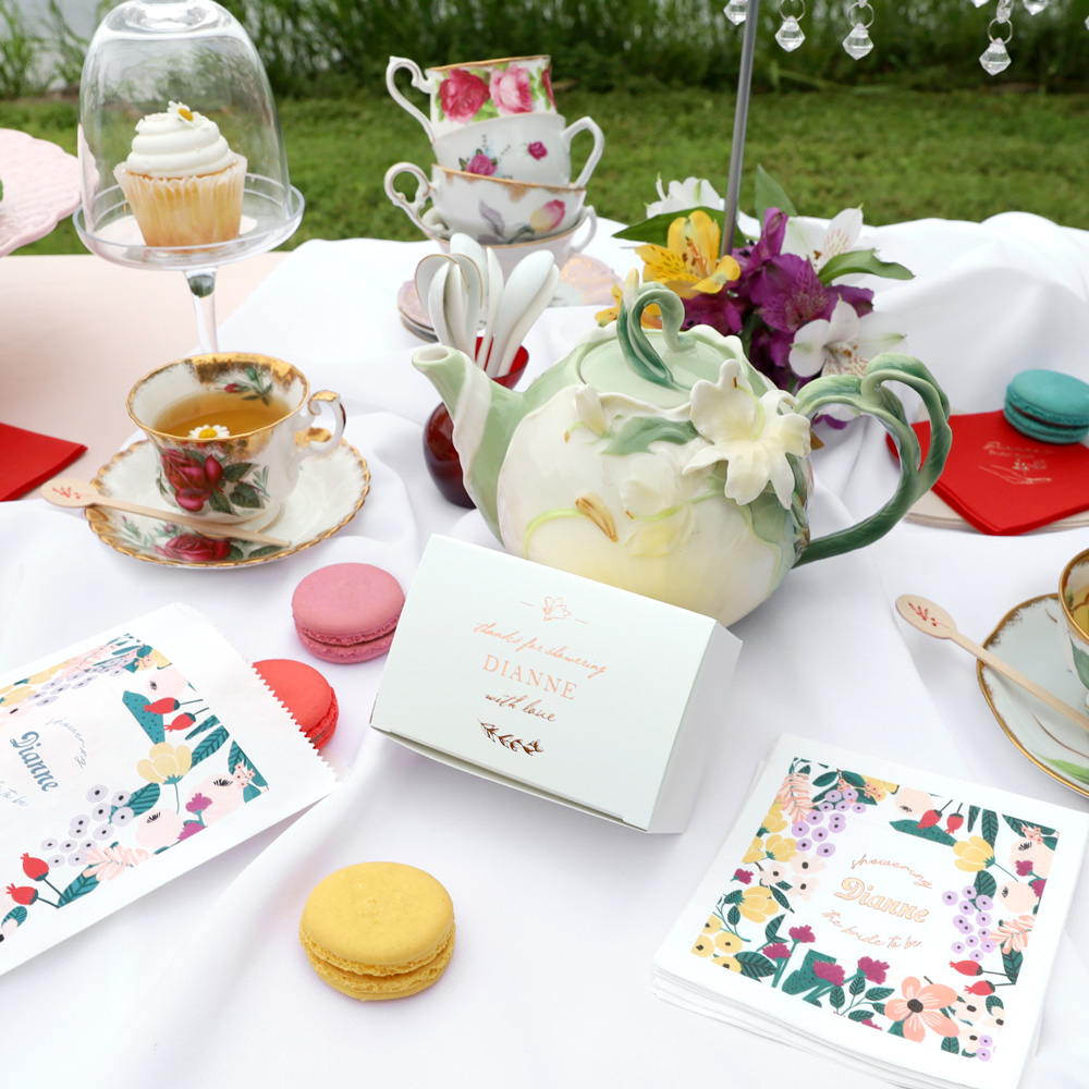 Tea Party Table Set up - Table with tea cup and teapot along with a cake box and cookie bag with macarons surrounding it